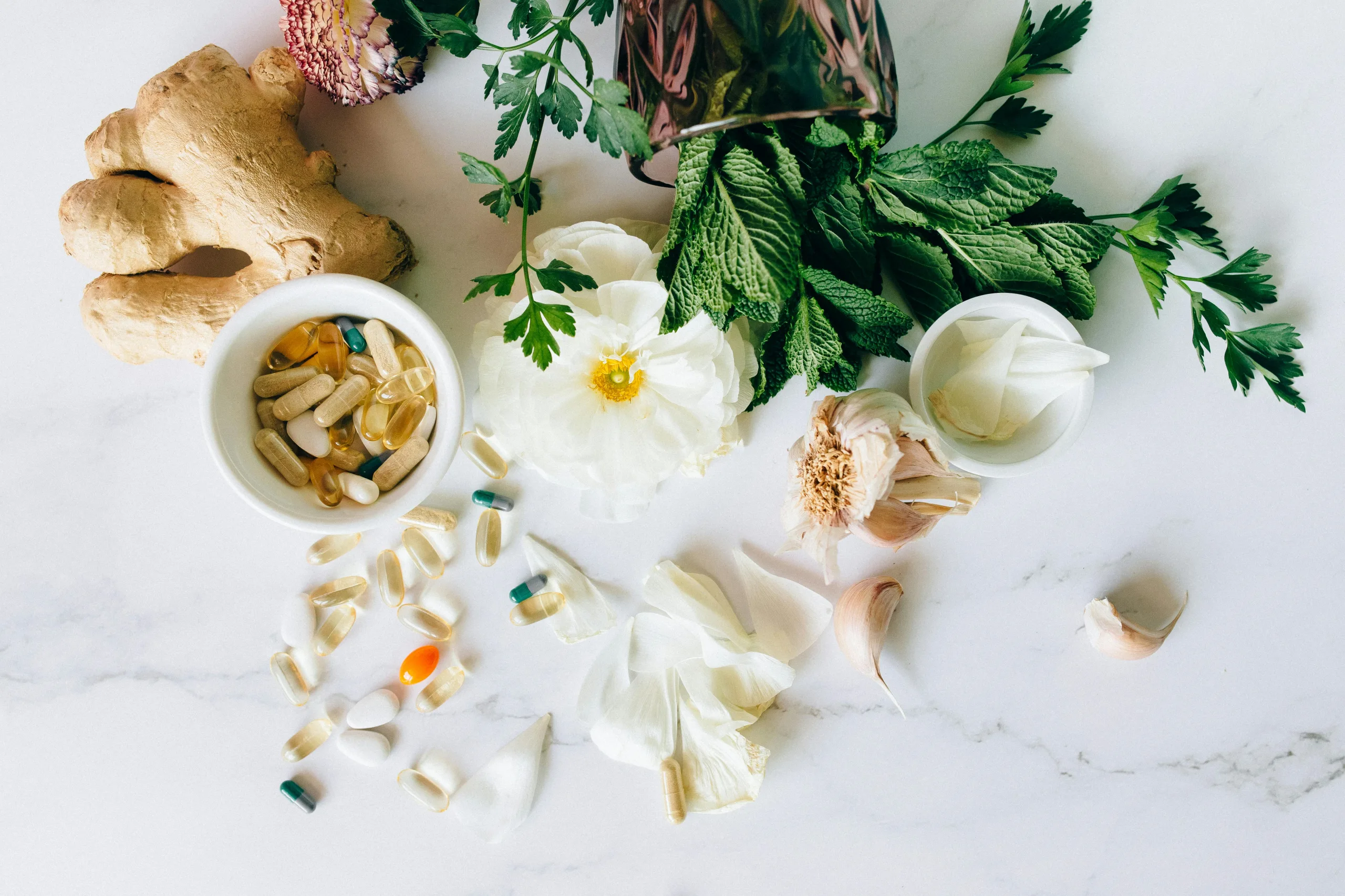 A flatlay of herbal supplements with fresh ginger, garlic, and leaves.